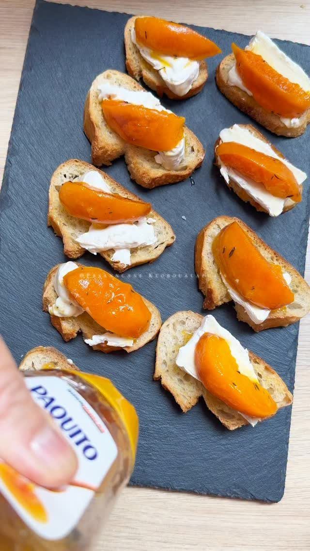 Toasted baguette slices topped with white cheese and apricot slices on slate platter