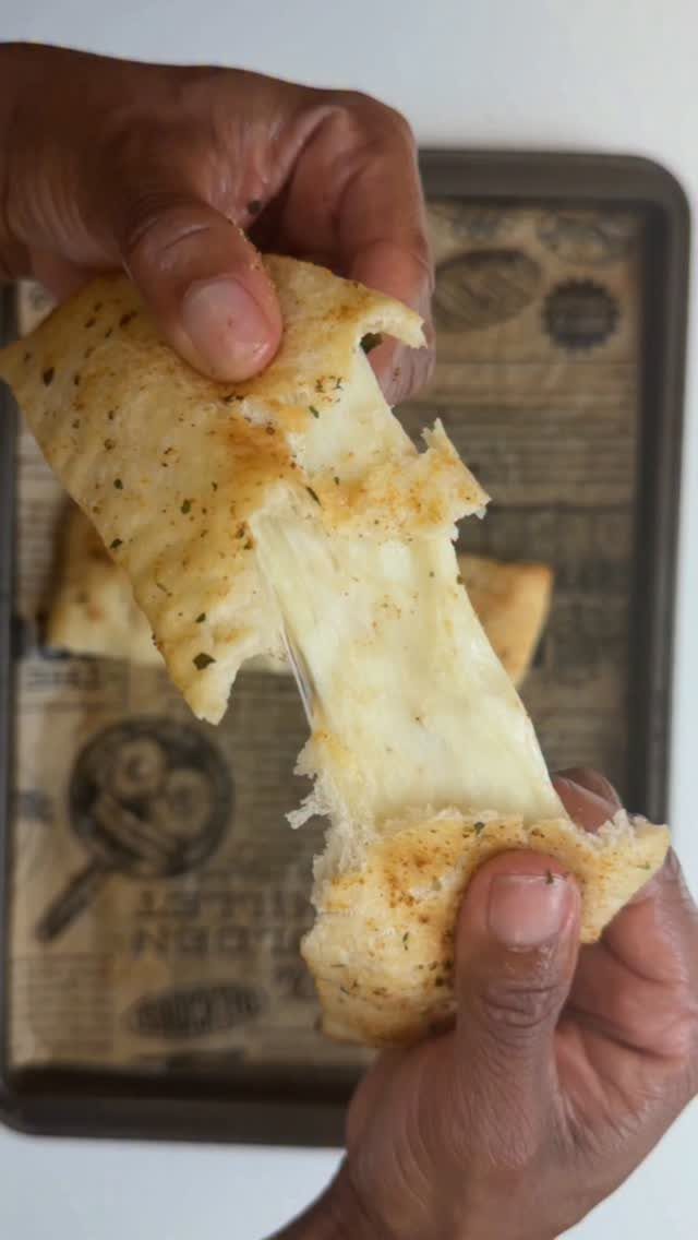 Hands pulling apart a piece of cheesy bread with melted cheese stretching between.