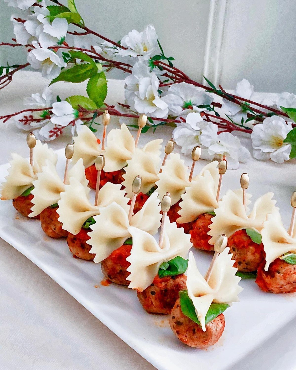 Meatballs topped with bow-tie pasta and basil on a white serving platter
