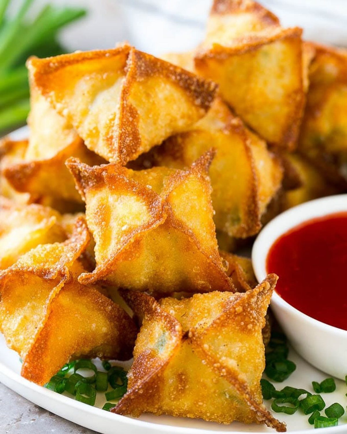 Fried crab ragoons on a white plate with red dipping sauce and scallions.