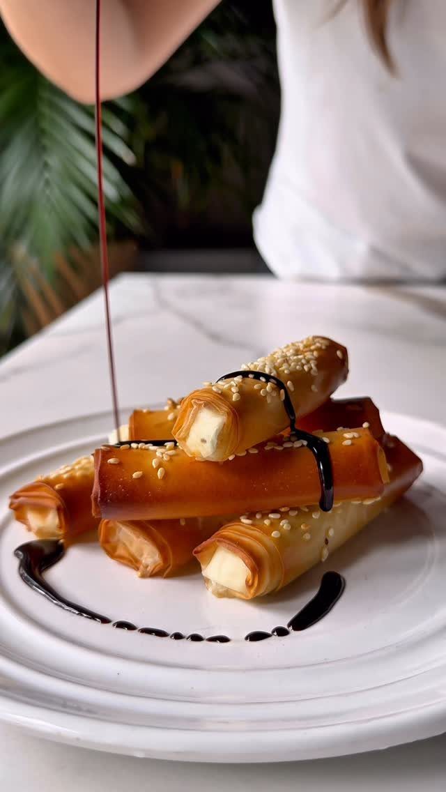 Cheese filled pastry rolls with sesame seeds and balsamic glaze on white plate