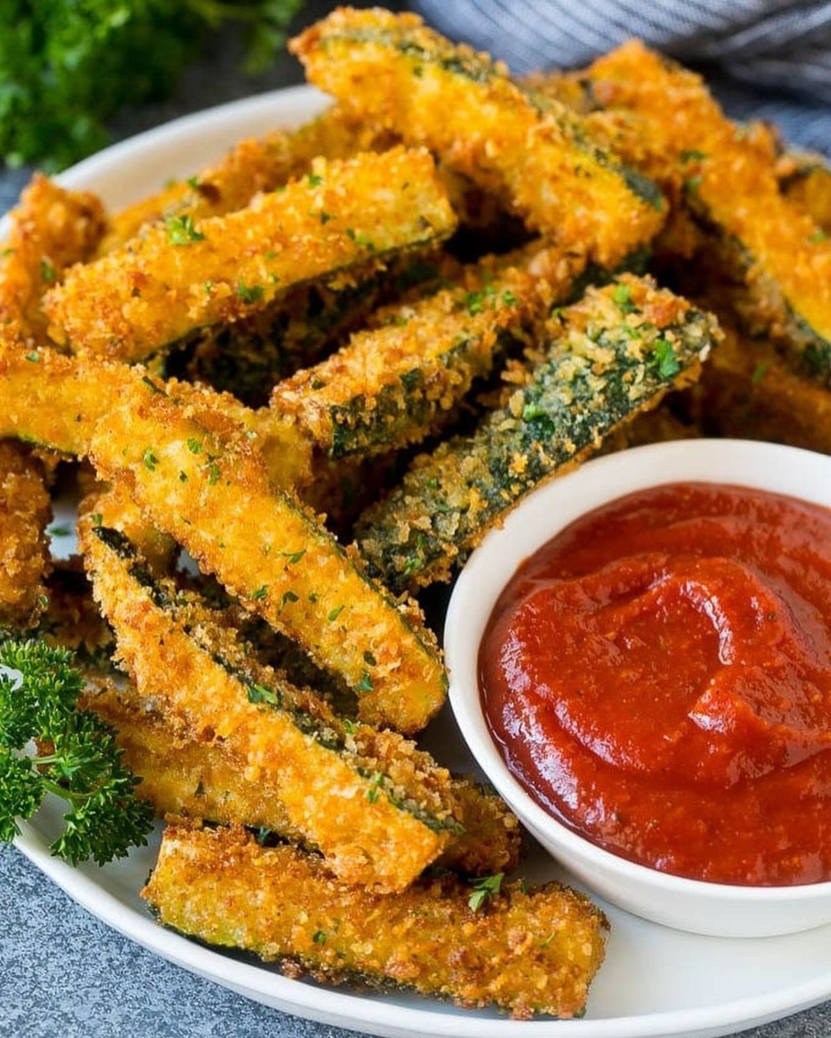 Fried zucchini sticks with breaded coating served with a side of marinara sauce.