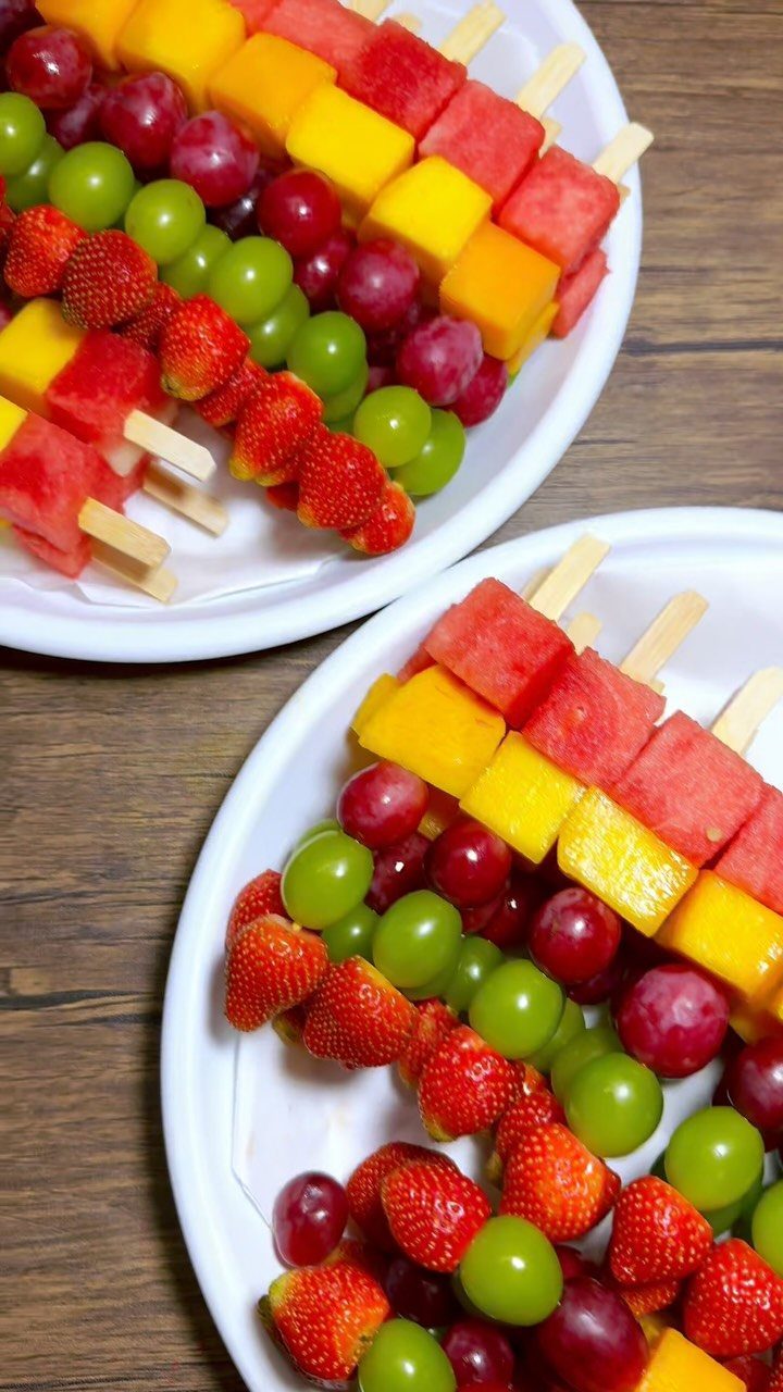 Fruit skewers with watermelon, mango, grapes, and strawberries on white plates.