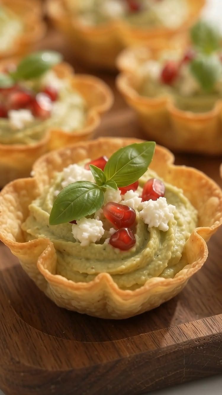 Green hummus in pastry cups topped with feta, pomegranate seeds, and basil leaves.