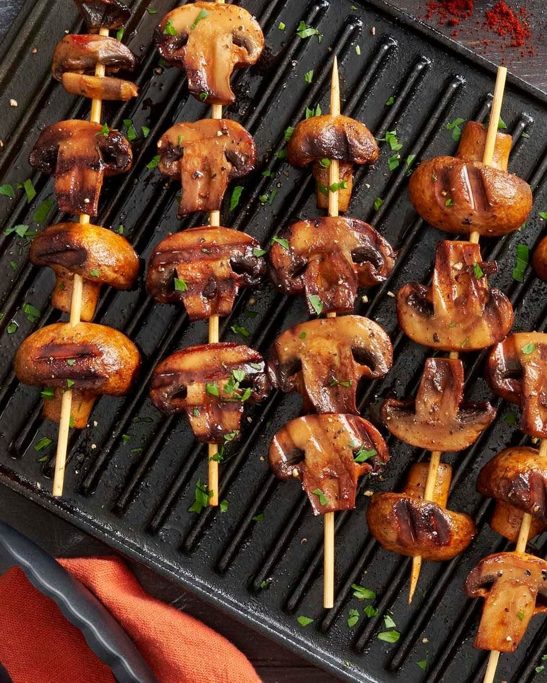 Grilled brown mushrooms on wooden skewers seasoned with herbs on a grill pan