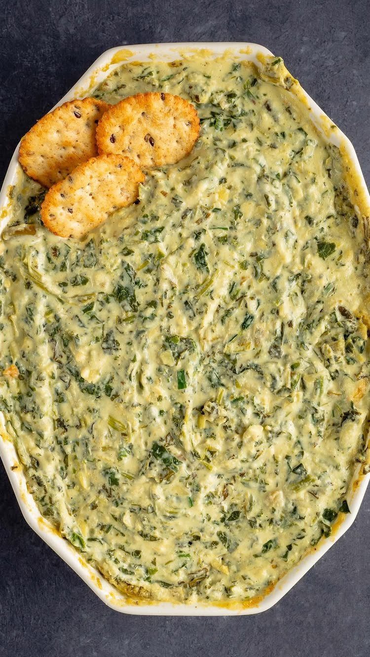 Spinach artichoke dip in a white baking dish with three round crackers.