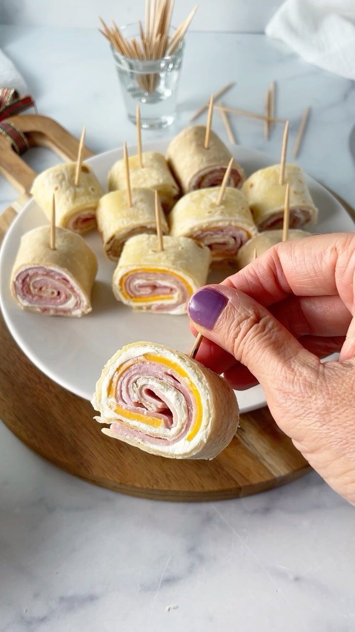Tortilla roll-ups filled with ham and cheese on a white serving plate.