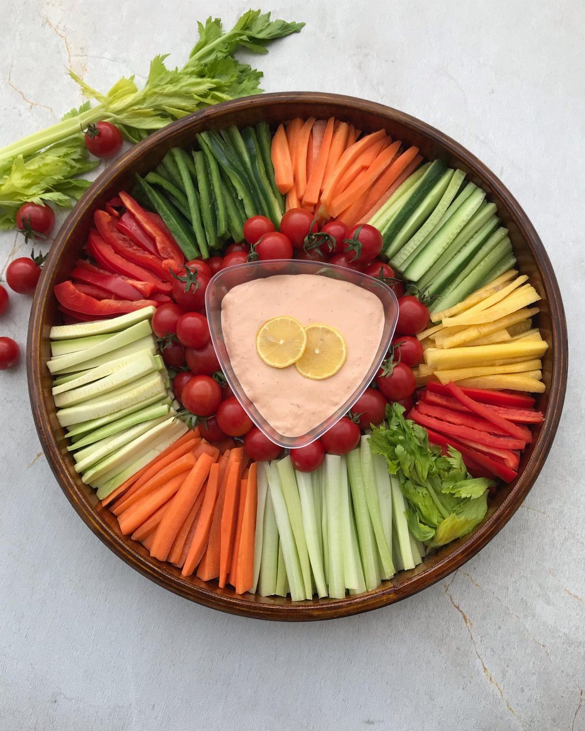 Vegetable platter with sliced peppers, carrots, and cucumbers surrounding a pink dip bowl.