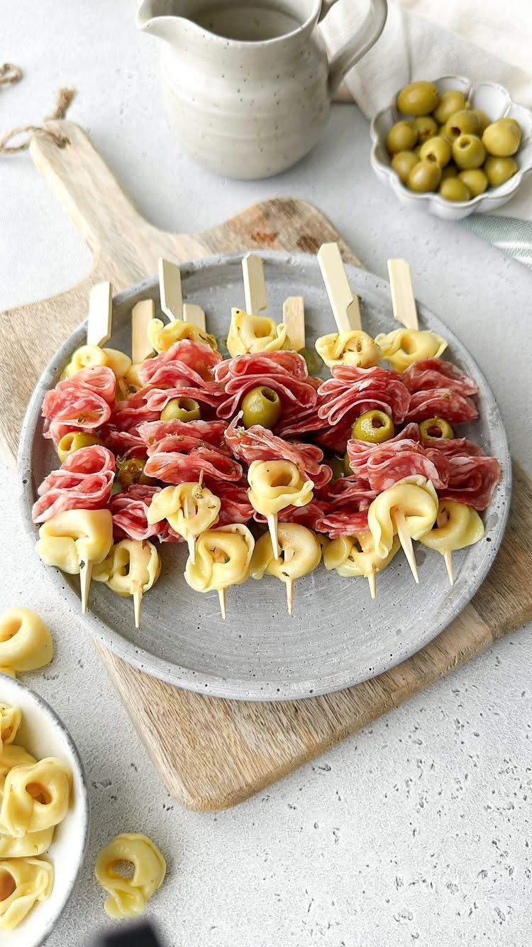 Salami and olive skewers with cheese on a grey plate and wooden board.