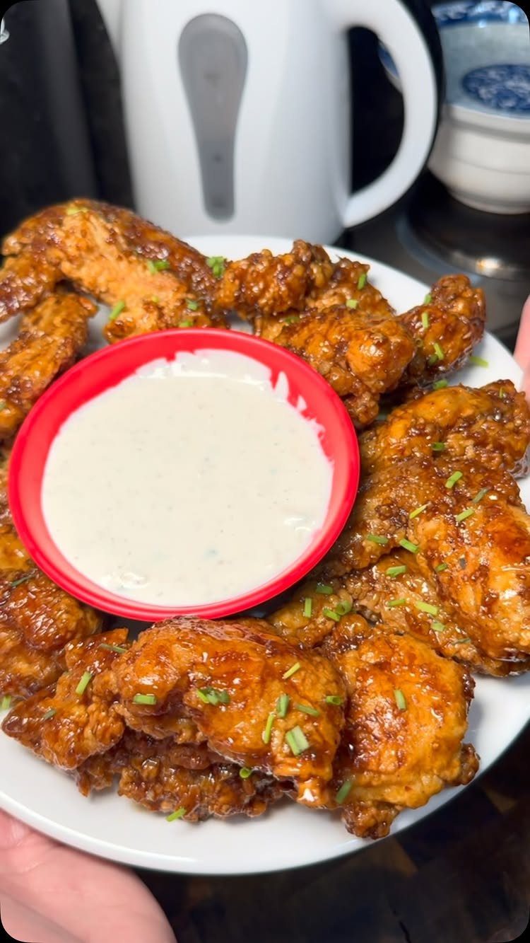 Glazed chicken wings with chives and a red bowl of creamy dipping sauce.