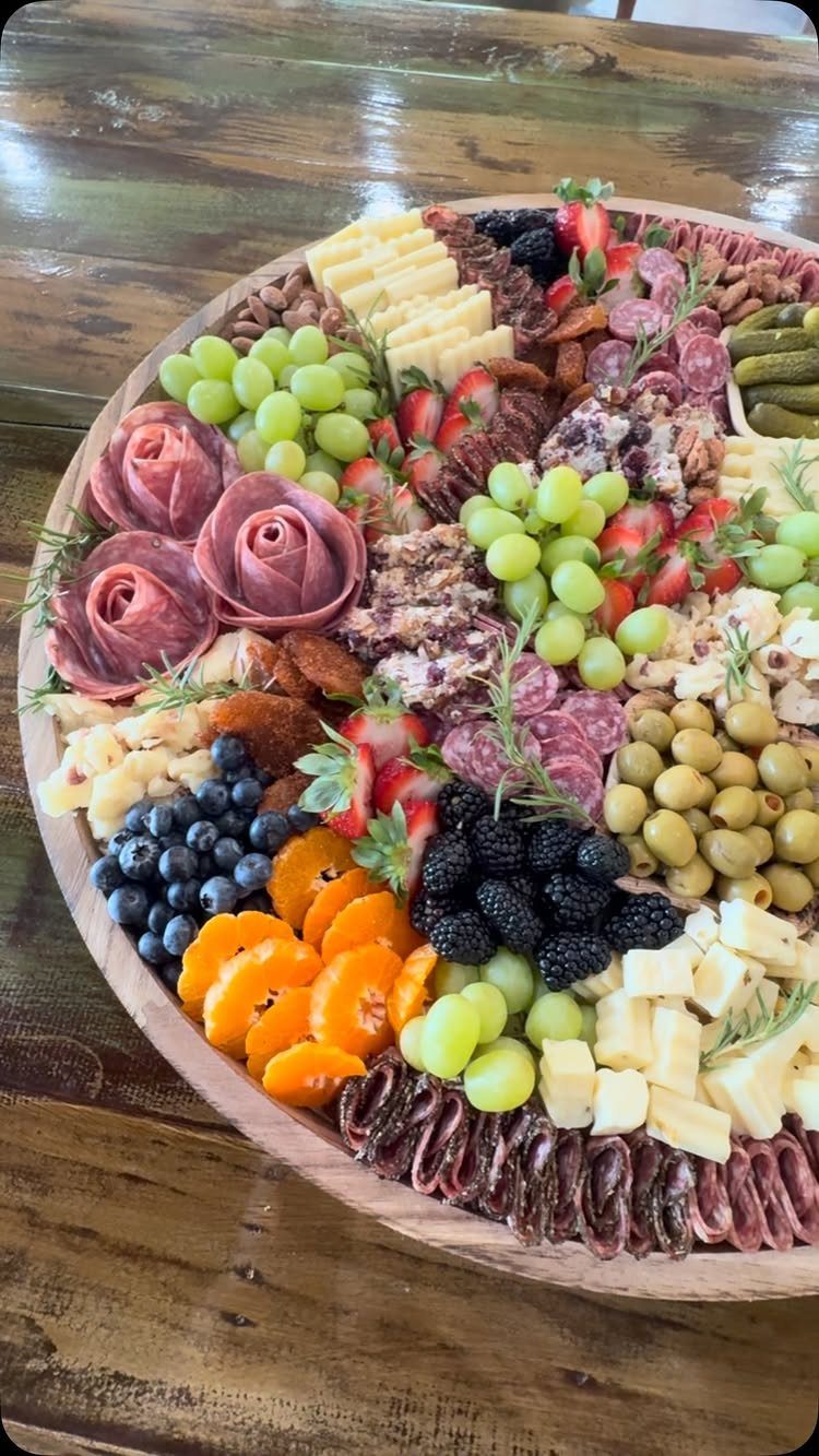 Charcuterie board with rolled meats, cheeses, grapes, berries, and olives on wooden platter.