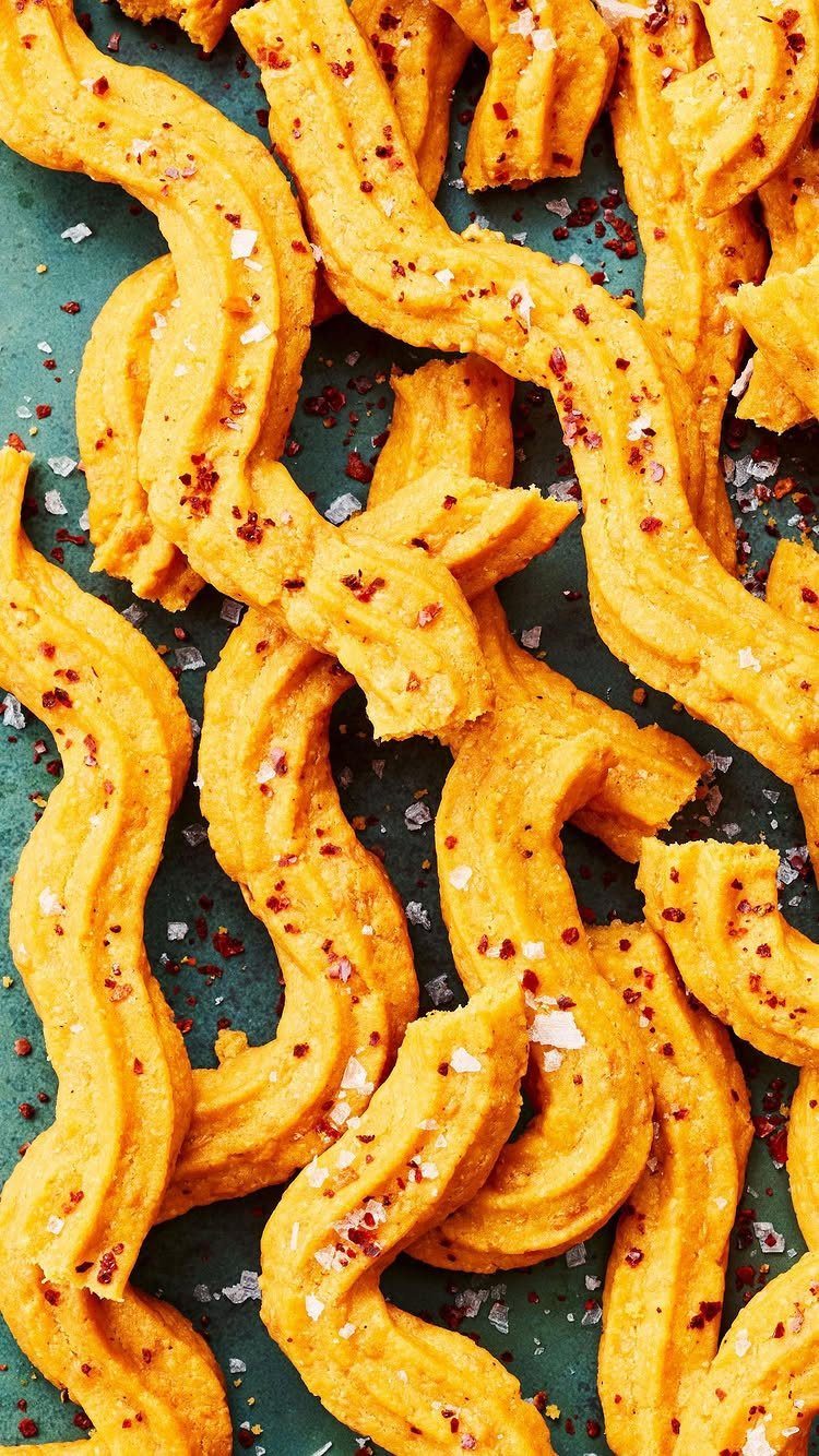 Wavy golden cheese straws with salt and red pepper flakes on teal background