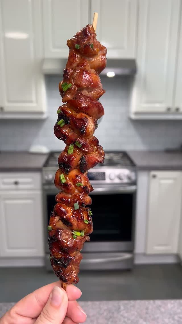 Glazed grilled chicken kebabs on a wooden skewer held in a hand.