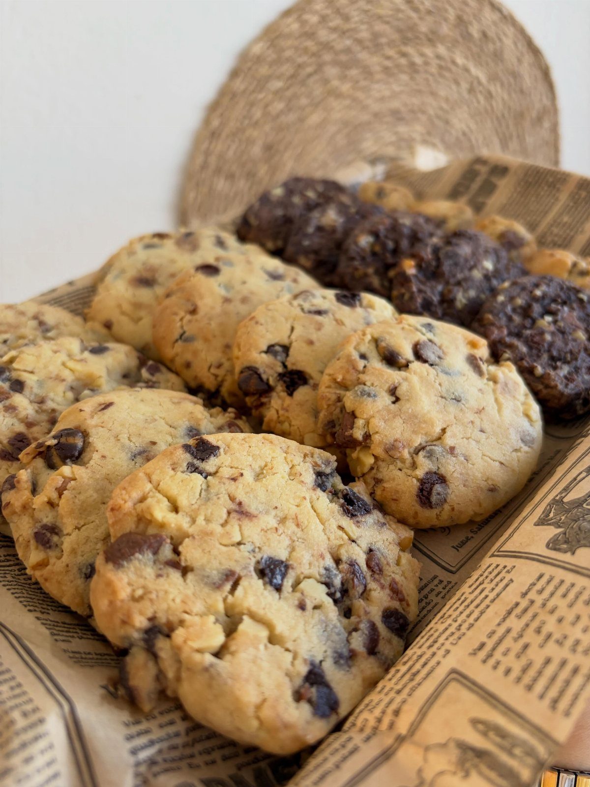 Chocolate chip cookies and dark chocolate cookies on newspaper-print parchment paper.