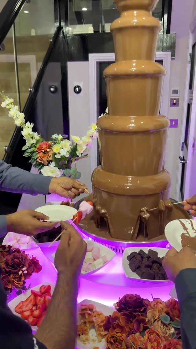 Chocolate fountain with strawberries and brownies being dipped by guests at a party.
