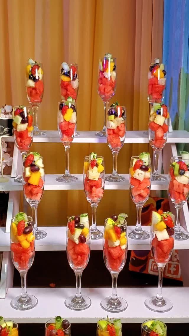 Champagne flutes filled with colorful chopped fruit on a white tiered display stand.