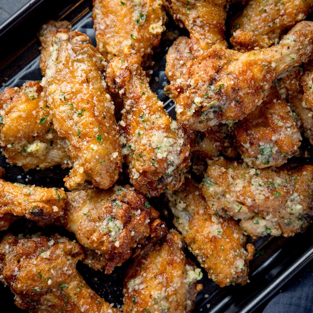 Garlic butter chicken wings with minced garlic and parsley on a black tray.