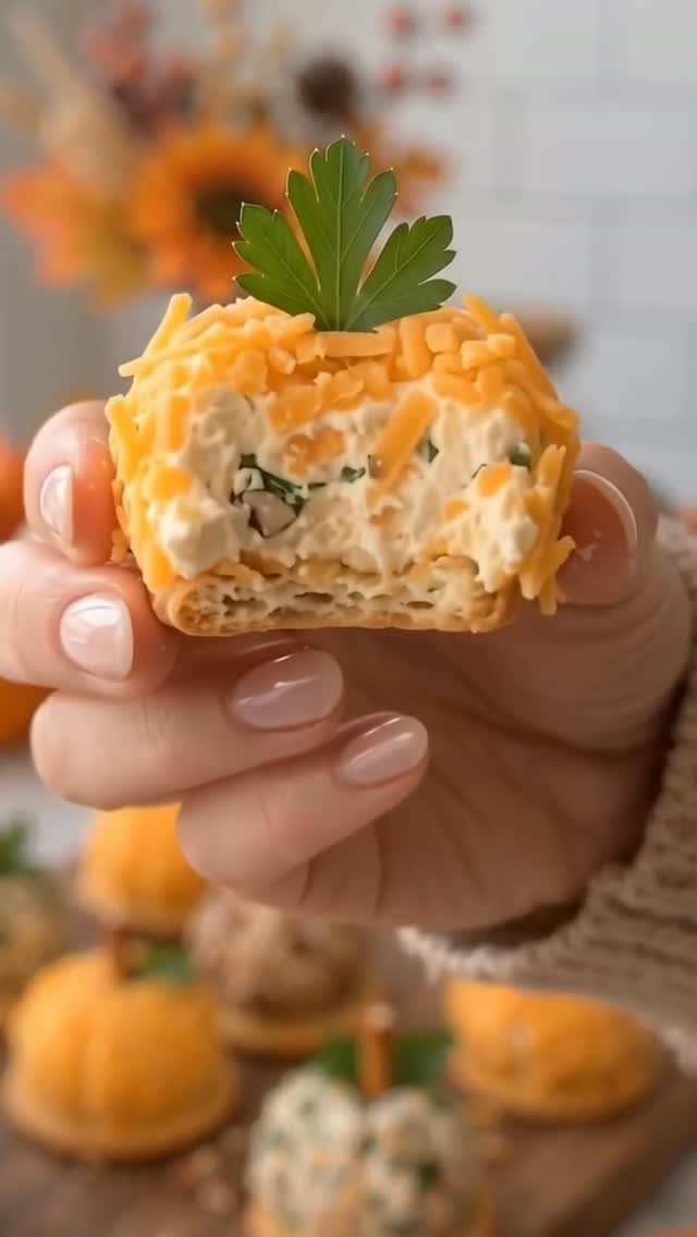 Mini cheese ball appetizer with shredded cheddar and parsley on a pretzel base.