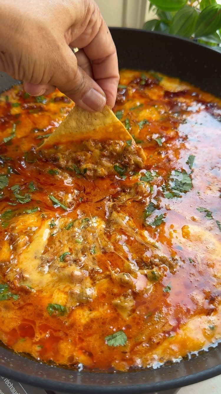 Tortilla chip dipping into a pan of melted cheese and spicy chorizo dip.