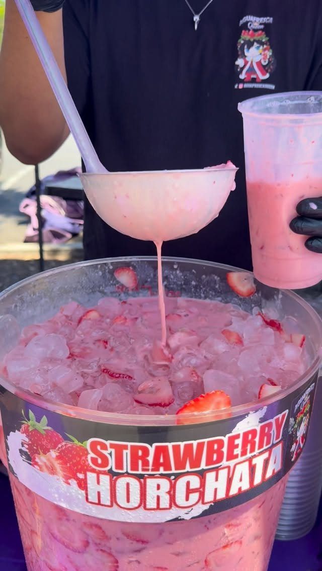 Pink strawberry horchata being ladled from a large ice-filled tub into a cup.