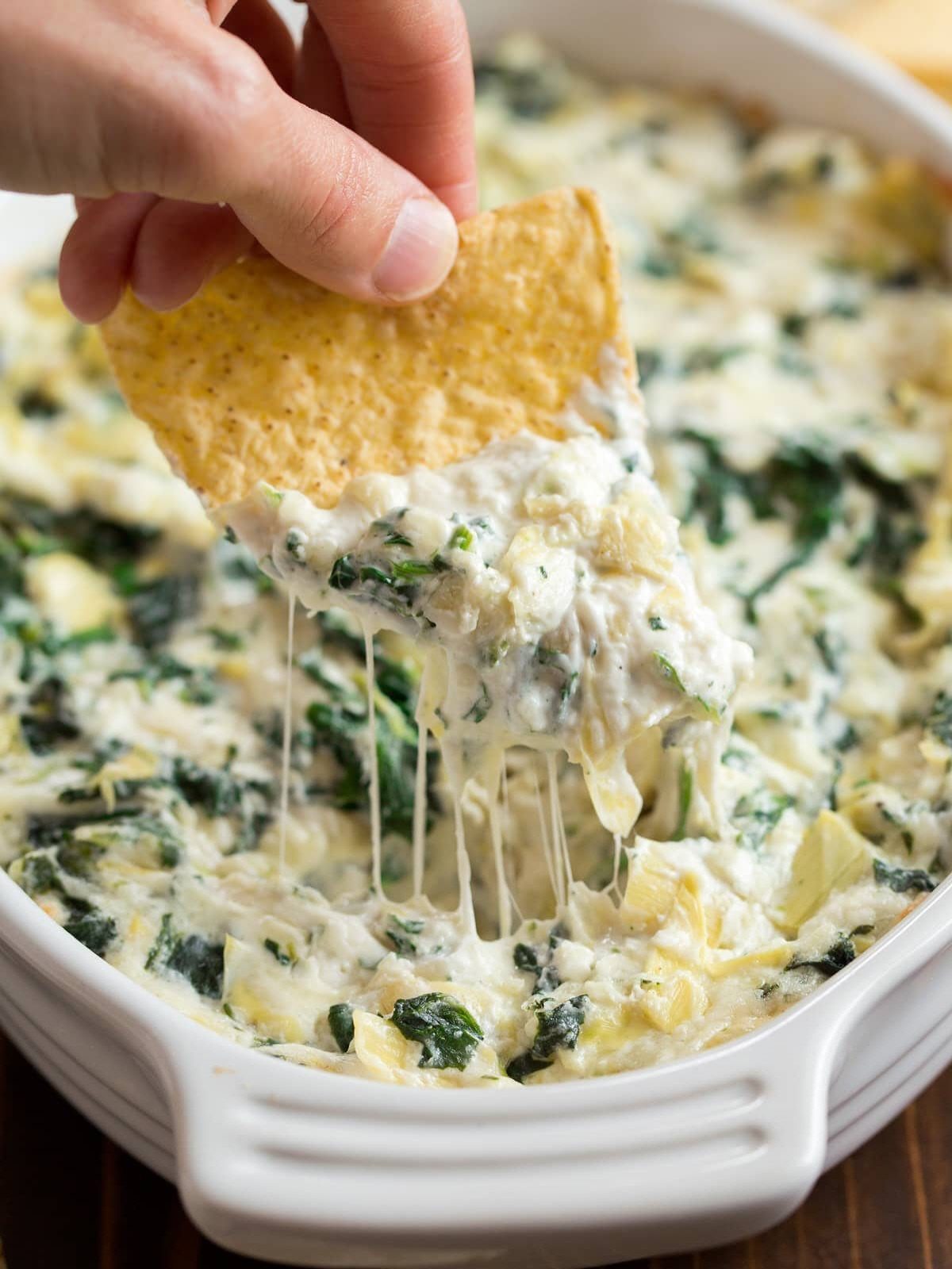 Tortilla chip dipping into creamy spinach and artichoke dip in a white dish