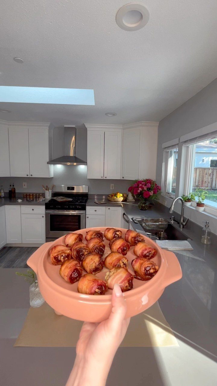 Bacon-wrapped dates served in a peach ceramic dish held in a modern kitchen.
