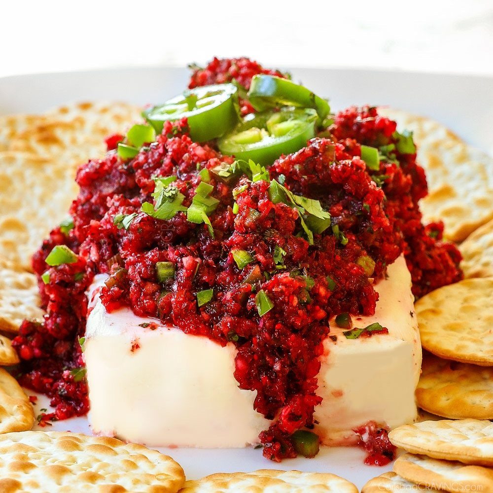 Cranberry basil dip on cream cheese served with crackers and jalapeño slices.