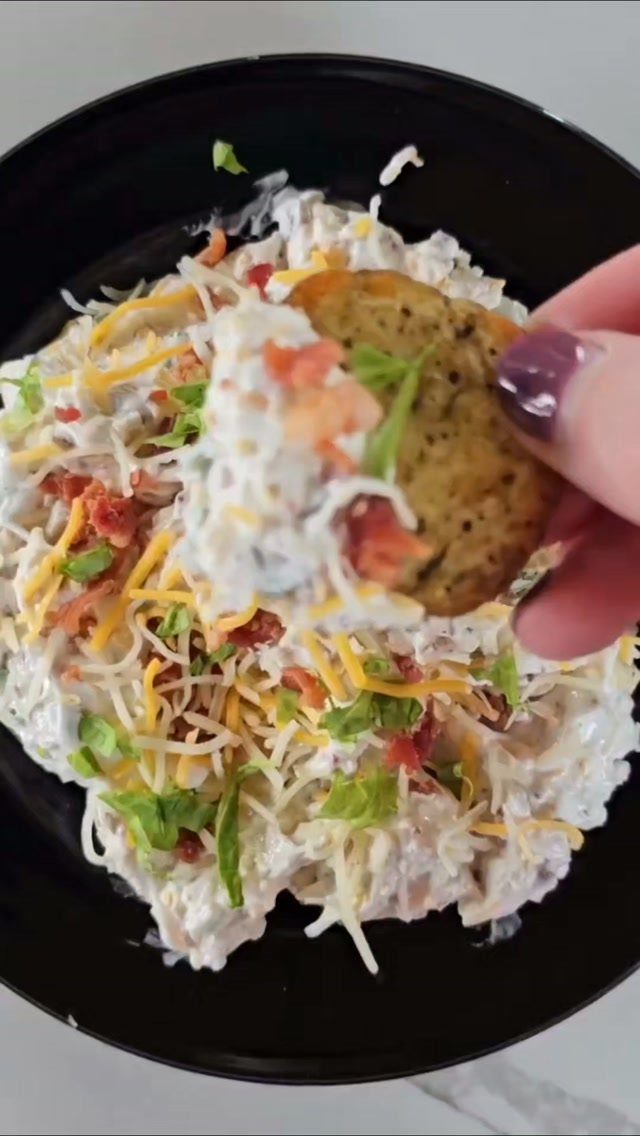 Creamy loaded baked potato dip with cheese and bacon in a black bowl.