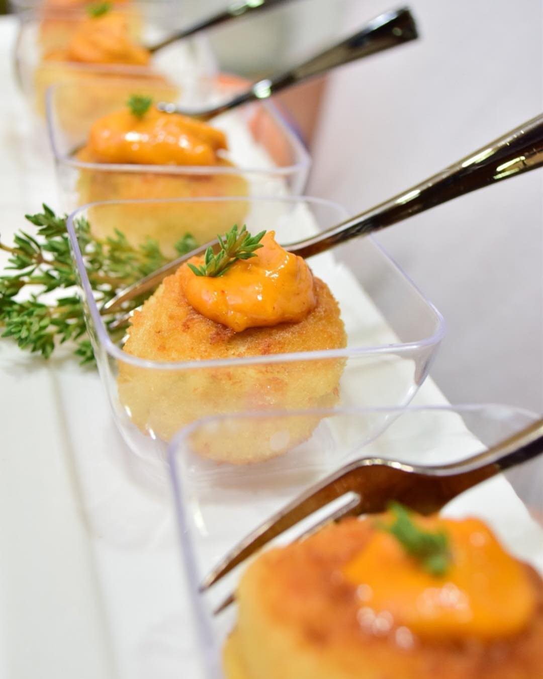Mini crab cakes topped with orange sauce in clear plastic appetizer cups