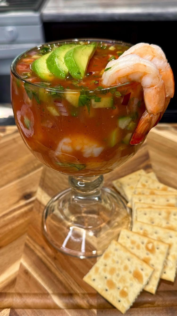 Shrimp cocktail in a glass goblet with avocado slices and side of crackers.
