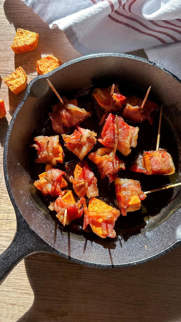 Bacon-wrapped sweet potato cubes with toothpicks in a black cast iron skillet.