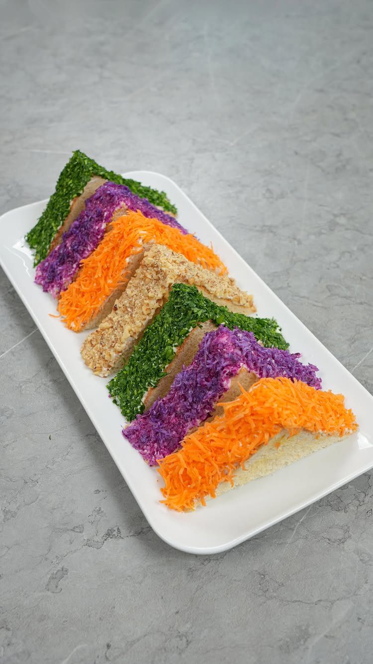 Colorful open-faced tea sandwiches with shredded vegetables on a white rectangular platter.