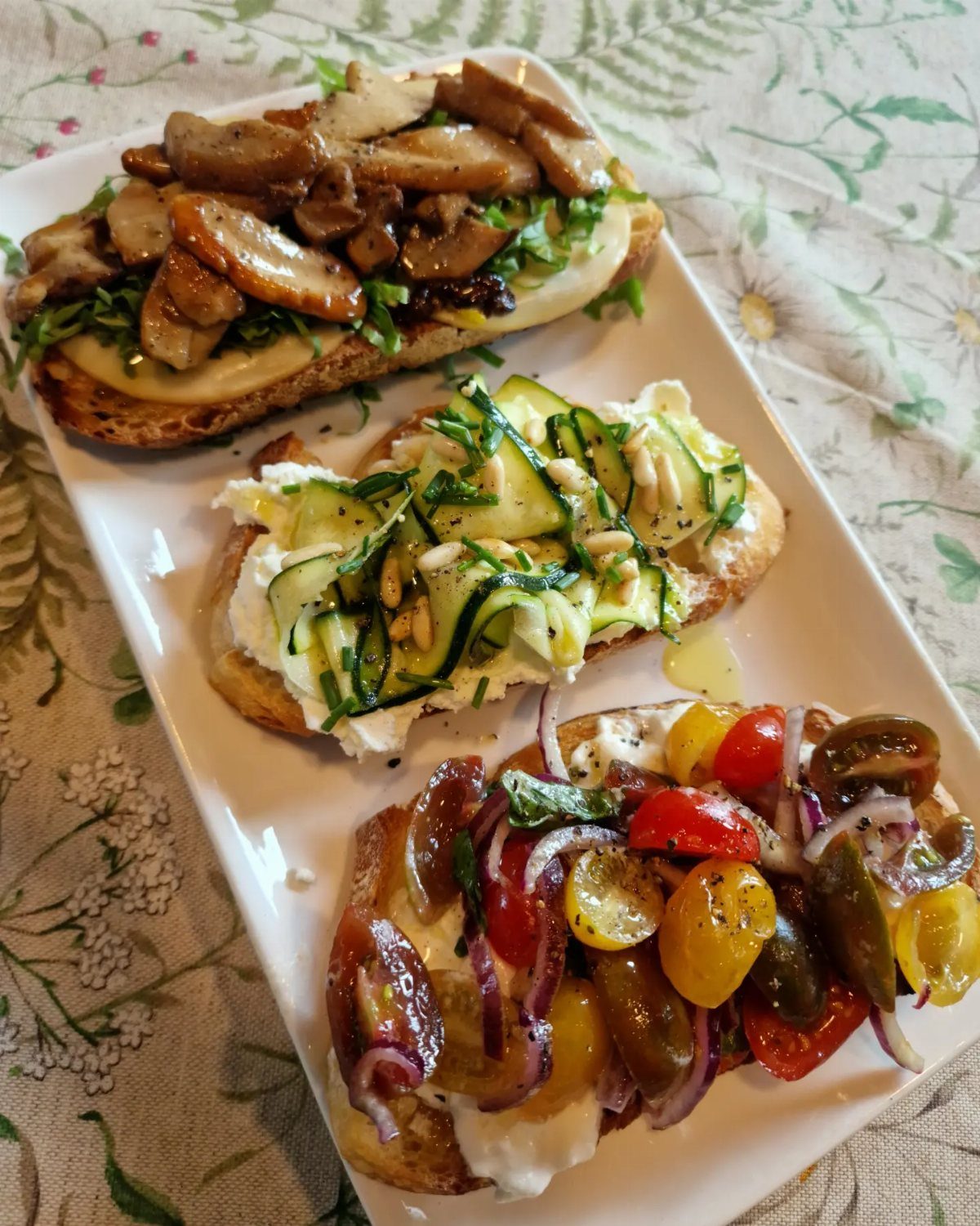 Three toasted baguette slices topped with mushrooms, zucchini, and cherry tomatoes on a platter.