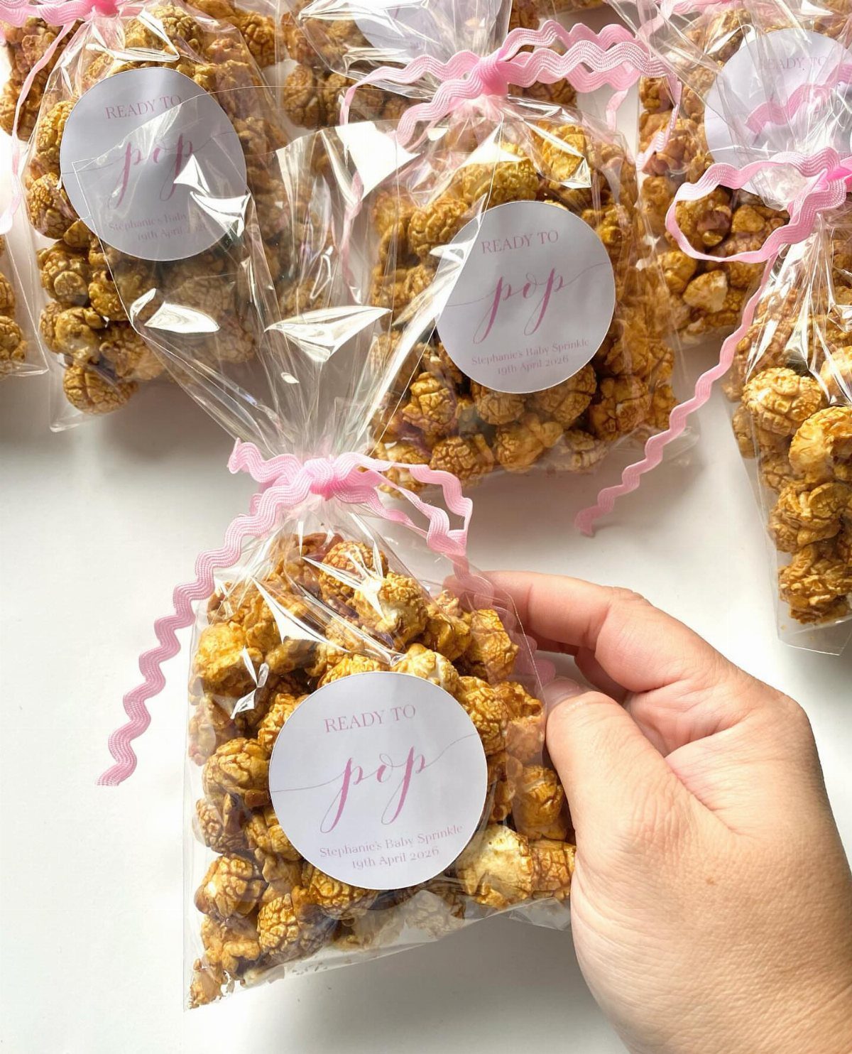 Caramel popcorn in clear bags with pink ribbons and circular white labels.