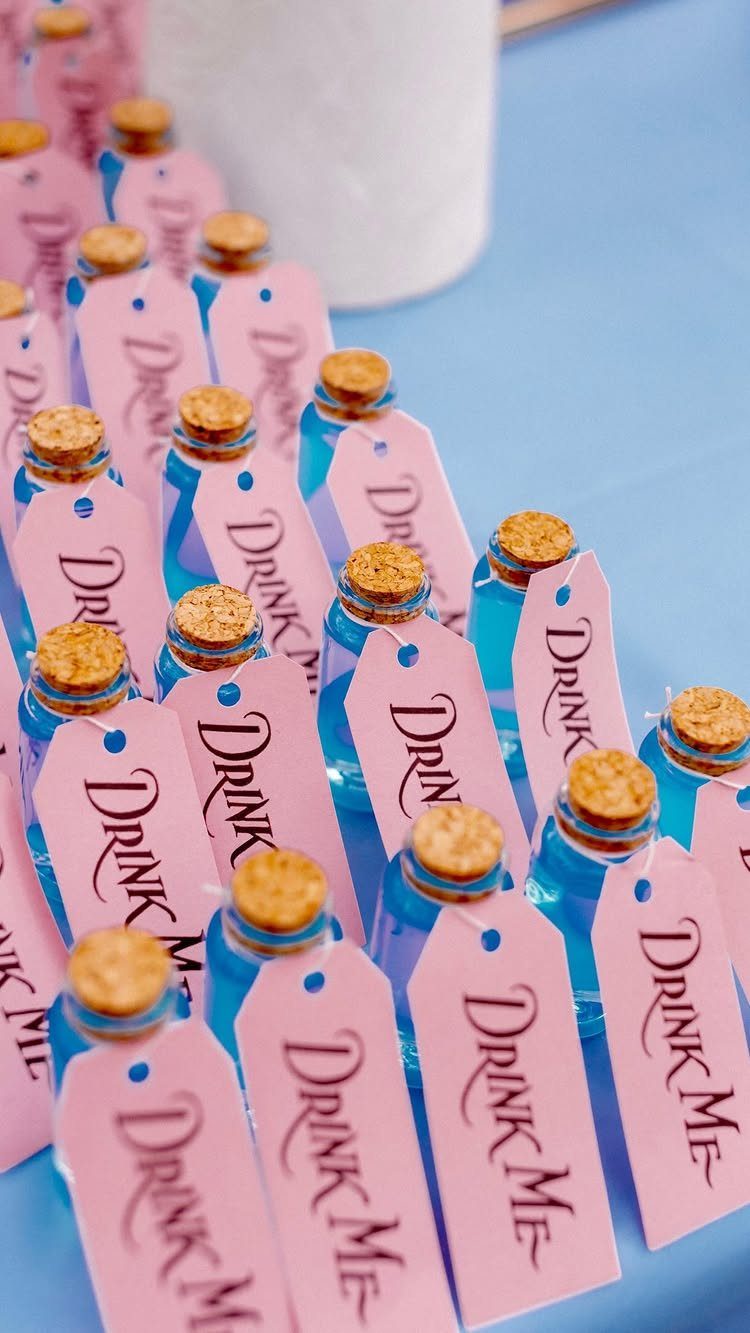 Blue liquid bottles with pink Drink Me tags hanging from the cork necks.
