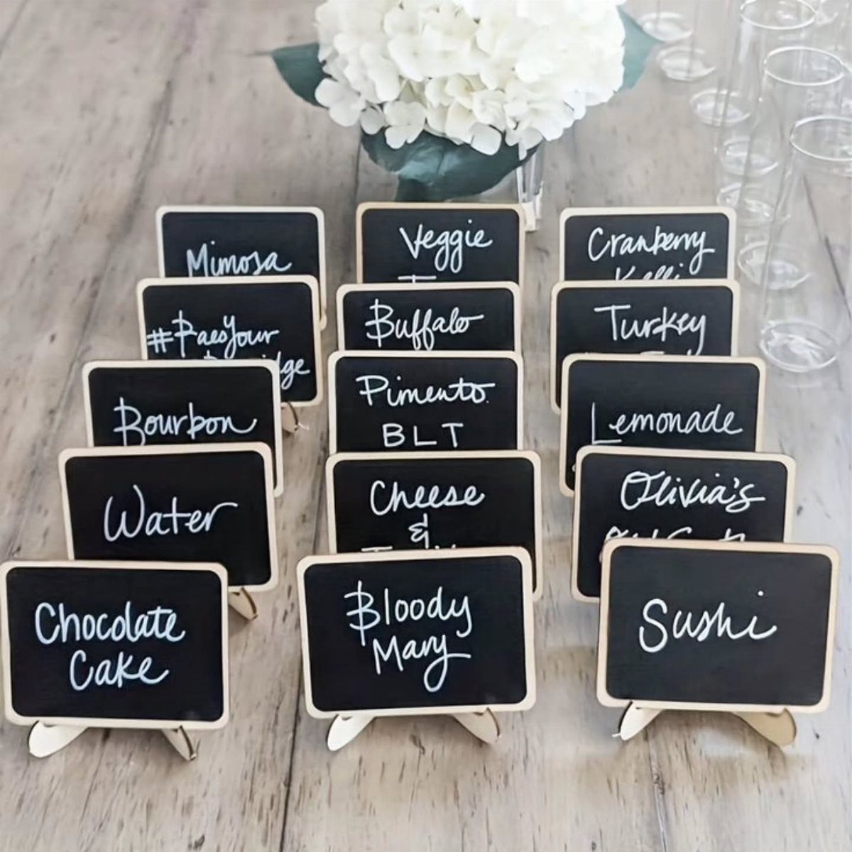 Mini chalkboards with white handwritten food and drink labels on small wooden easels.