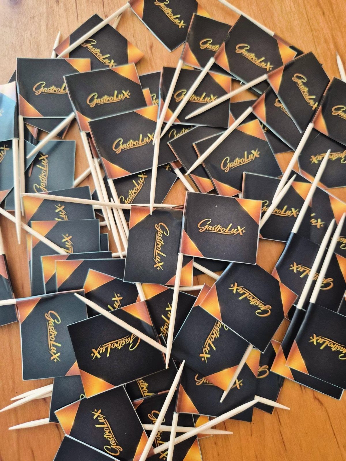 Black paper flags with gold text on wooden toothpicks scattered on wood.