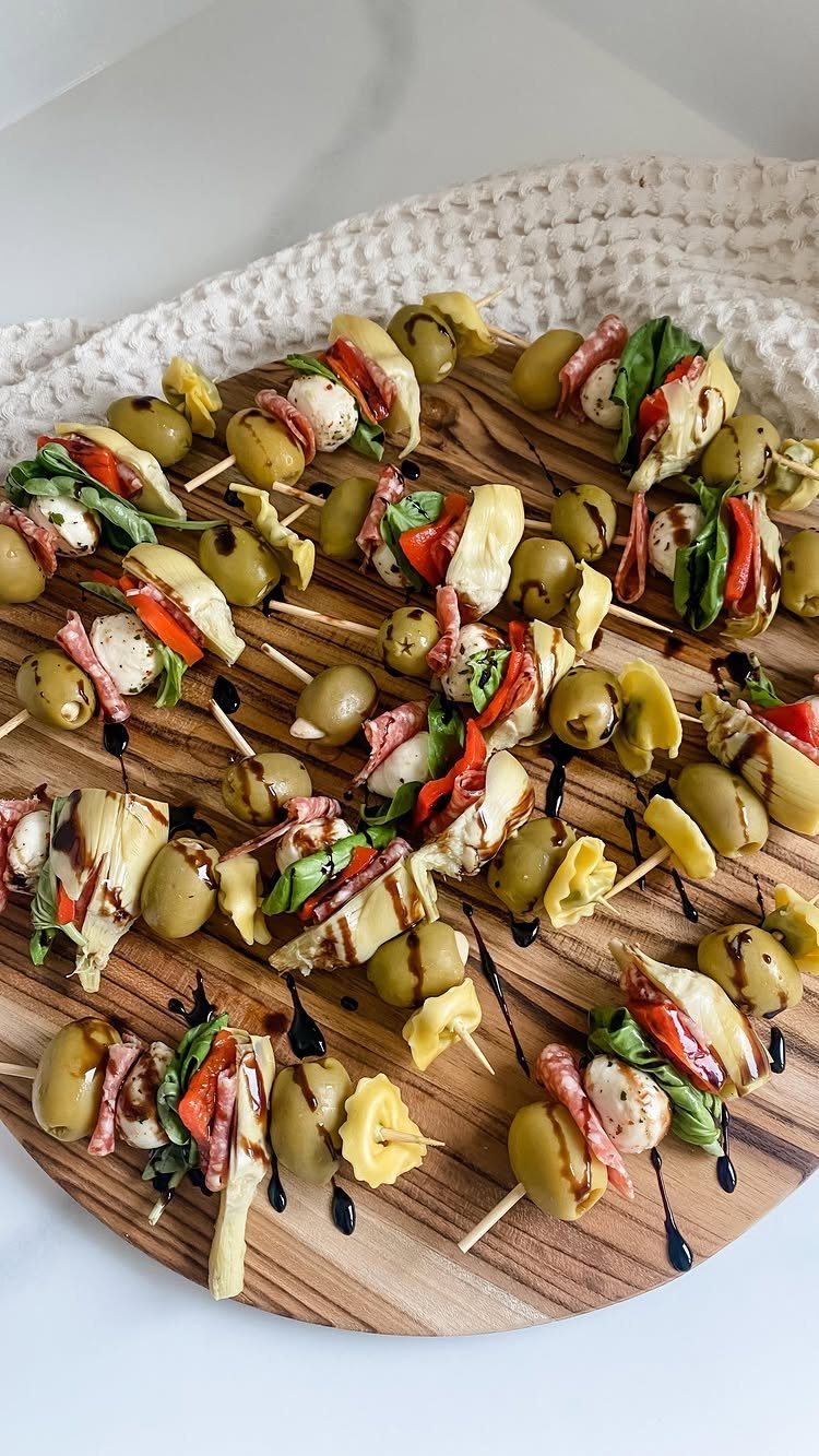 Antipasto skewers with olives, cheese, and meats drizzled with balsamic on wooden board.