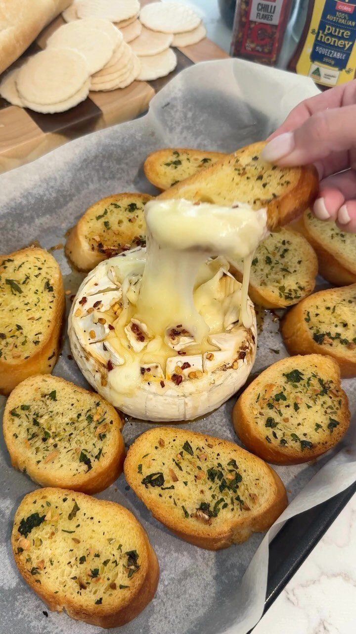 Melted baked brie cheese with toasted garlic bread slices on parchment paper.
