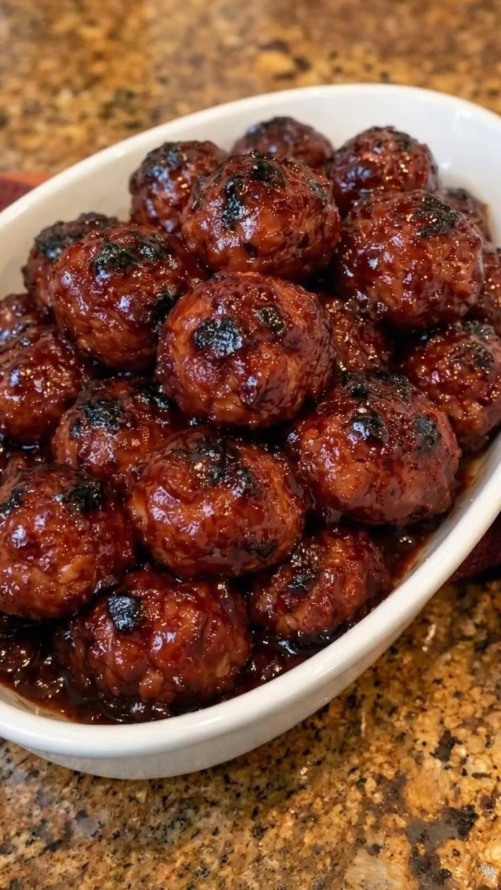 Glazed meatballs in a dark sauce served in a white oval dish.