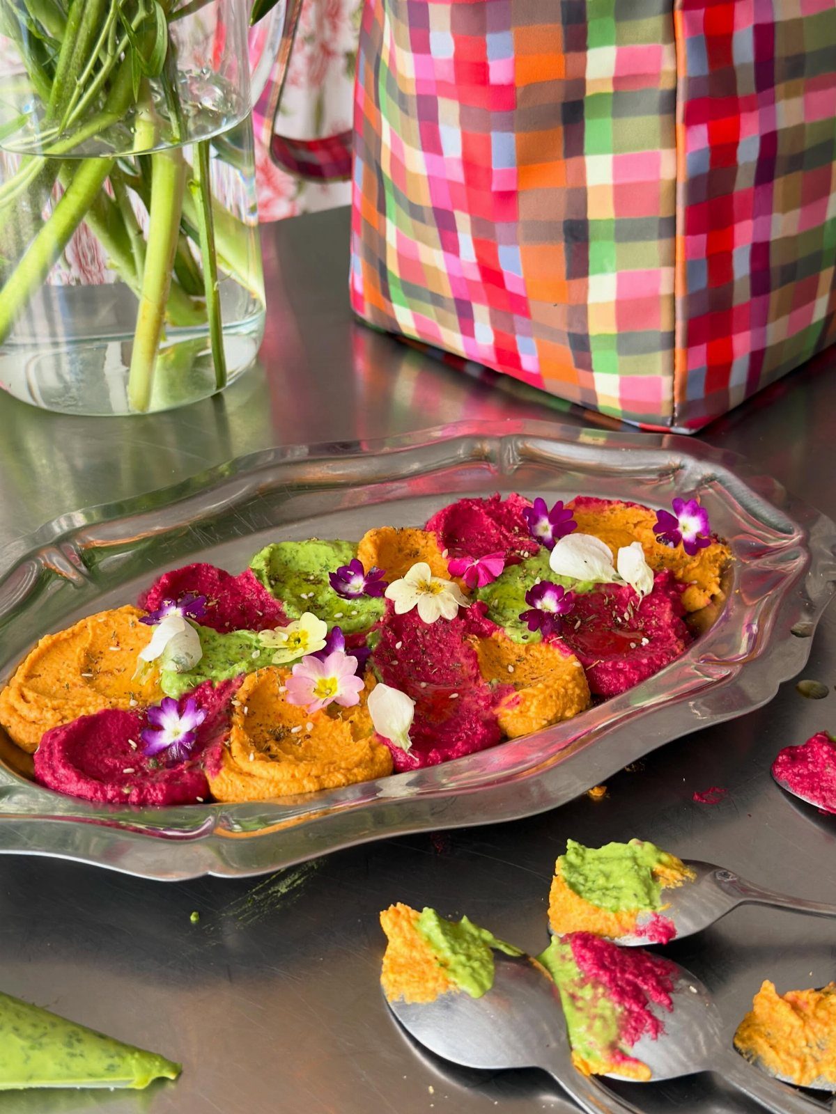 Colorful scoops of hummus garnished with edible flowers on a silver platter.