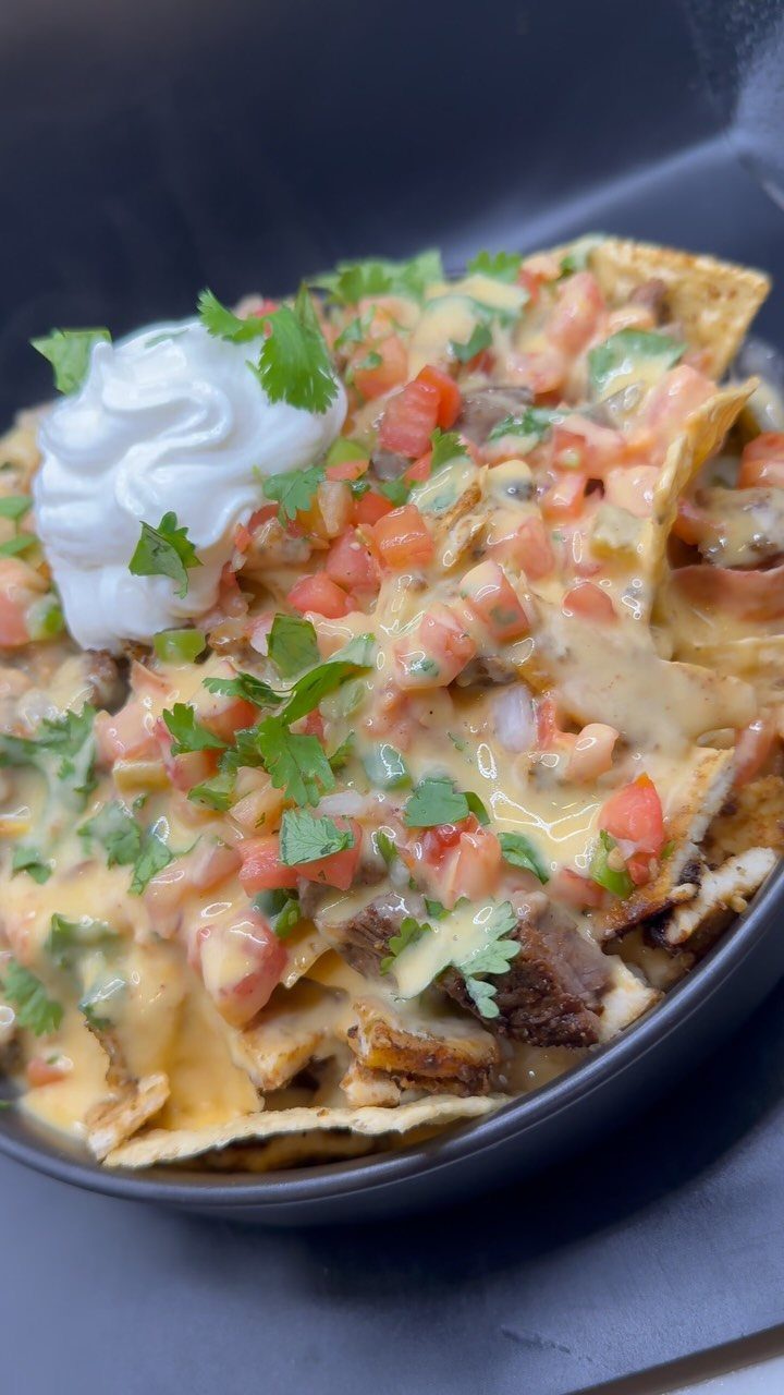 Loaded nachos with melted cheese, tomatoes, cilantro, and sour cream in a bowl.