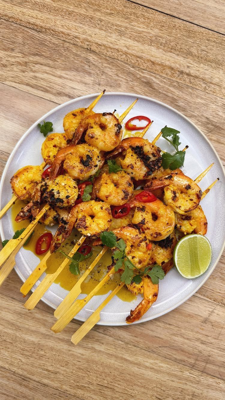 Grilled shrimp skewers with chili and cilantro on a white plate with lime.