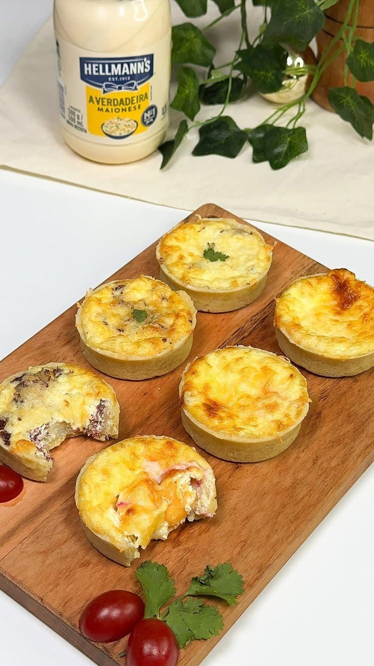 Mini quiches with melted cheese on a wooden board next to mayonnaise.