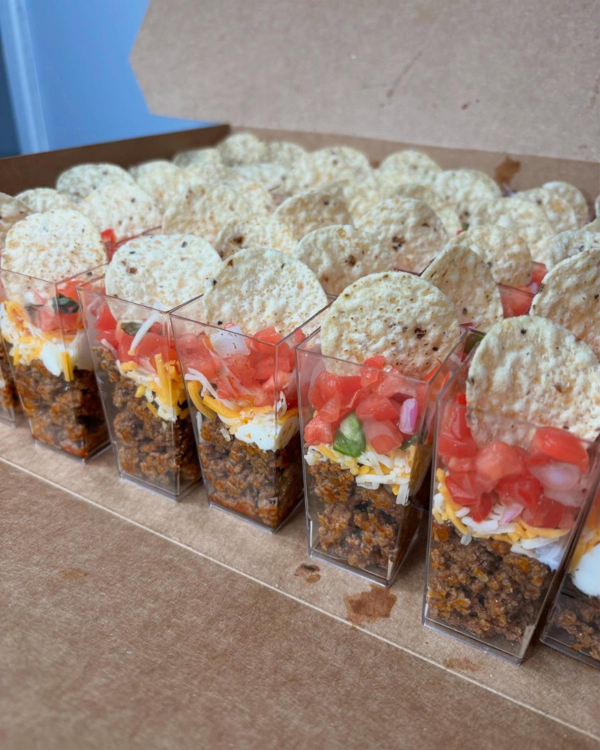 Mini taco cups with layered meat, cheese, and tomatoes topped with tortilla chips.
