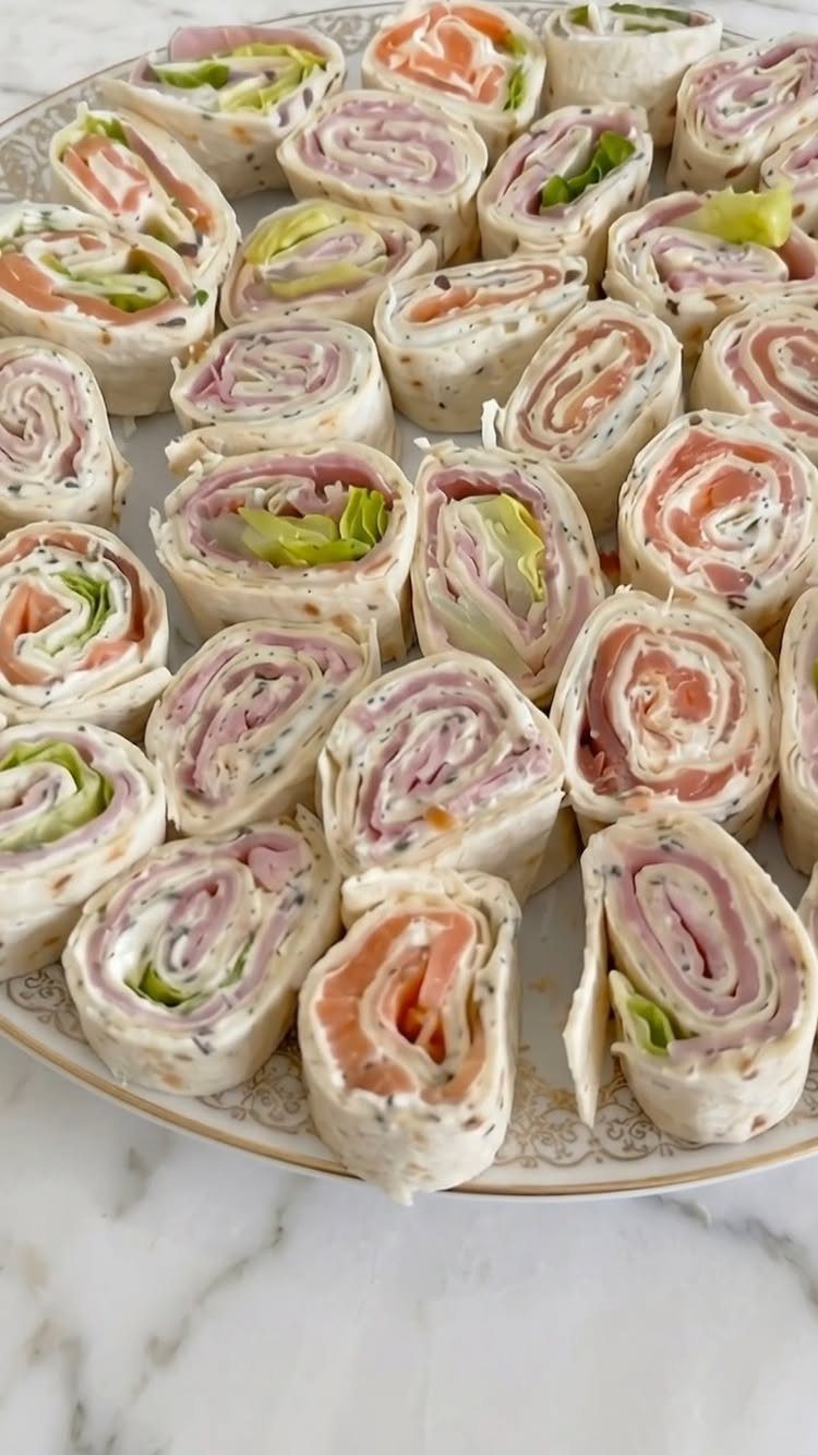 Pinwheel sandwiches with salmon and ham arranged on a white decorative platter.