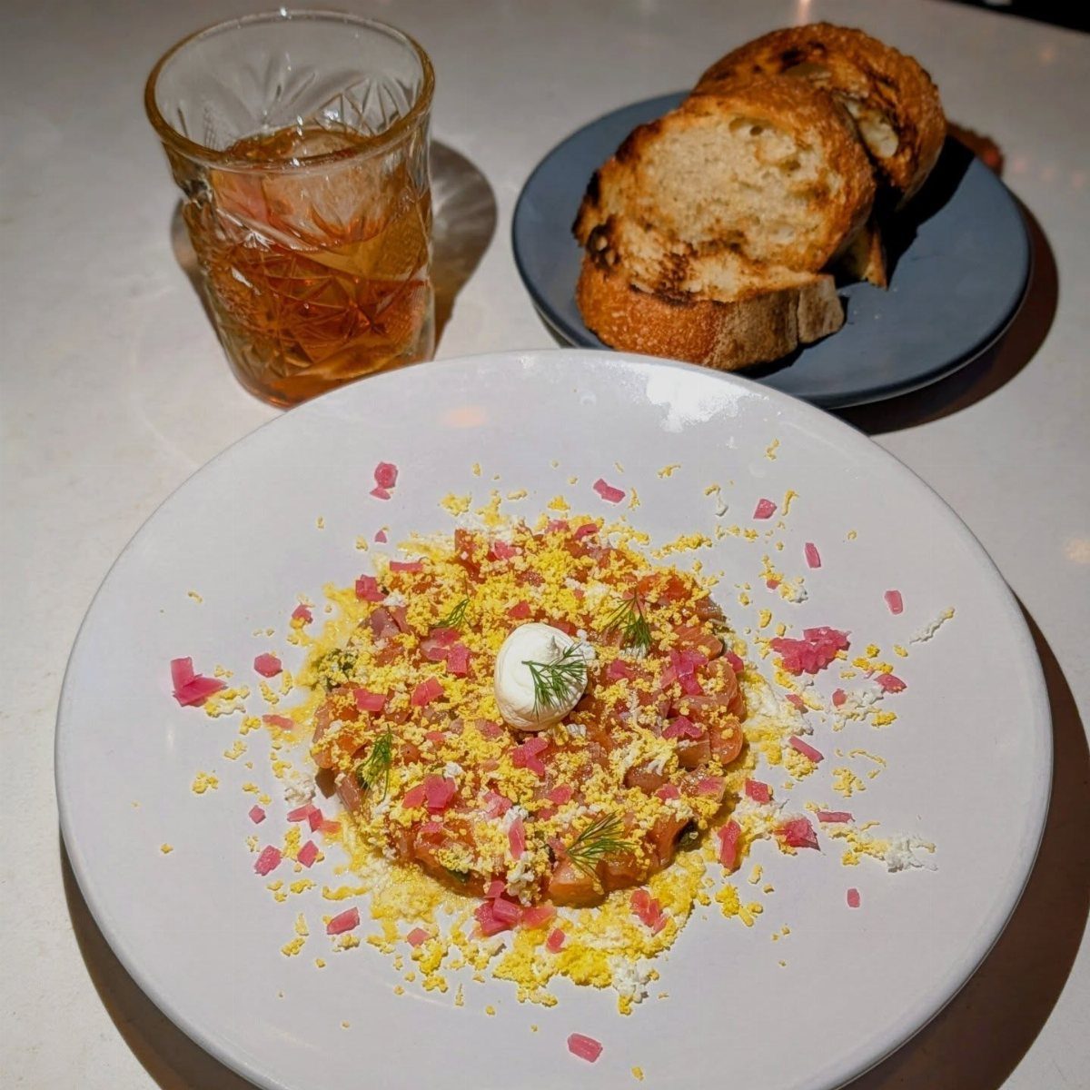 Salmon tartare with cream and dill on a white plate with toasted bread.