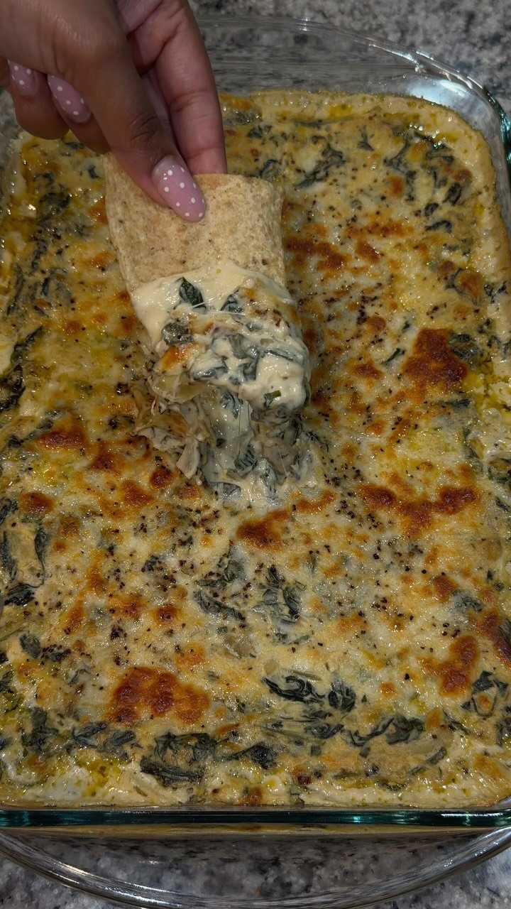 Tortilla chip dipping into a creamy baked spinach artichoke dip in glass dish