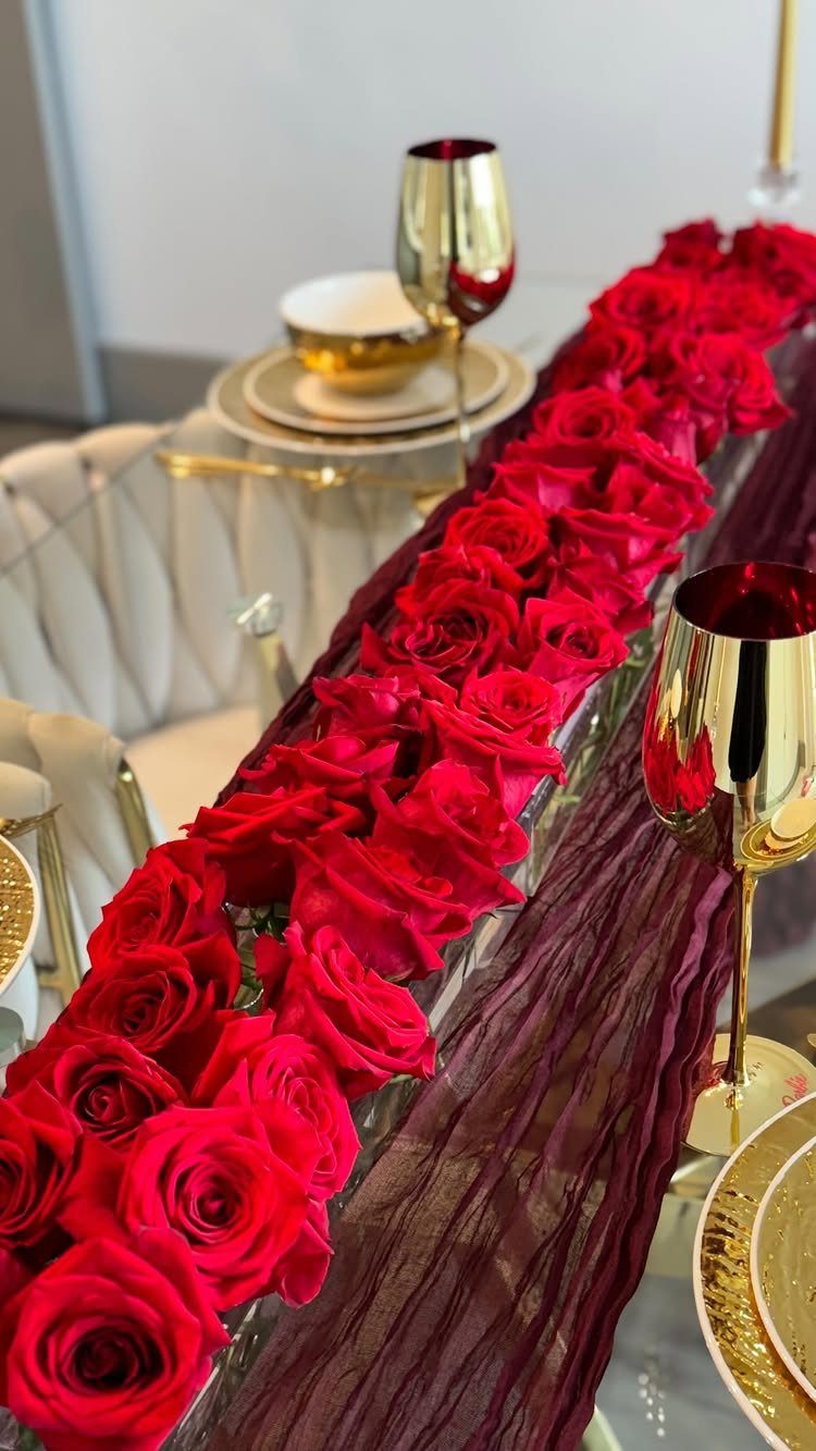 Red rose runner and gold tableware on a table with burgundy fabric.