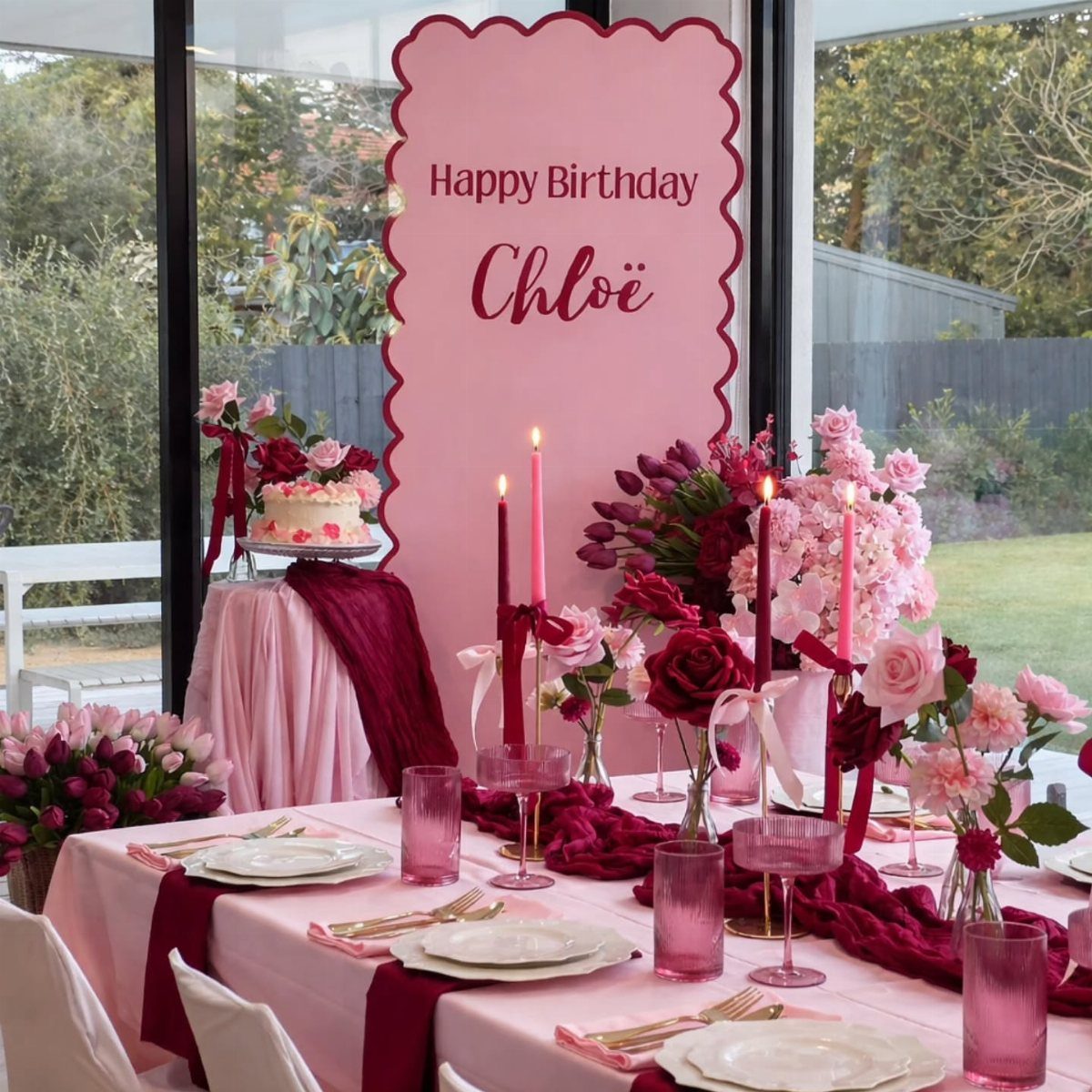 Party table with pink tablecloth, burgundy runner, pink candles, and red roses.